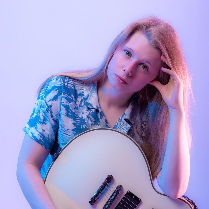 A blonde guitarist with a blue shirt and white electric guitar.
